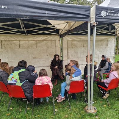 Figure sitting under a tent with children sitting around figure