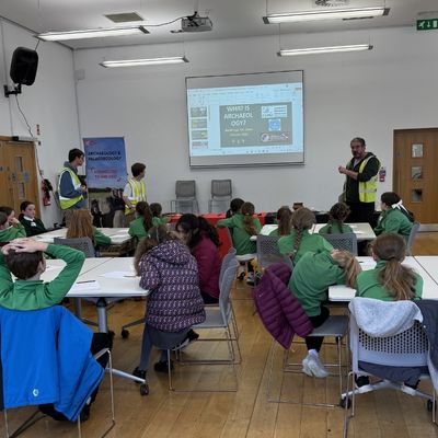 three individuals taking a session with 30 school children in green uniform
